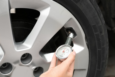 Woman checking car tire pressure with air gauge, closeup