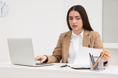 Unhappy young female intern at table in office