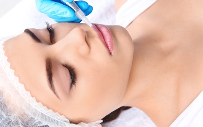 Photo of Young woman getting permanent makeup on lips in beautician salon