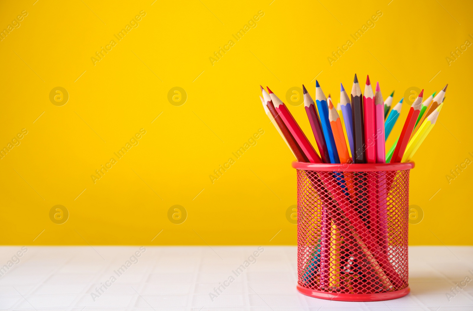 Photo of Many colorful pencils in holder on light table against yellow background, space for text