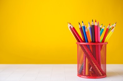 Many colorful pencils in holder on light table against yellow background, space for text