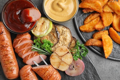 Delicious grilled sausages and vegetables on grey table, flat lay