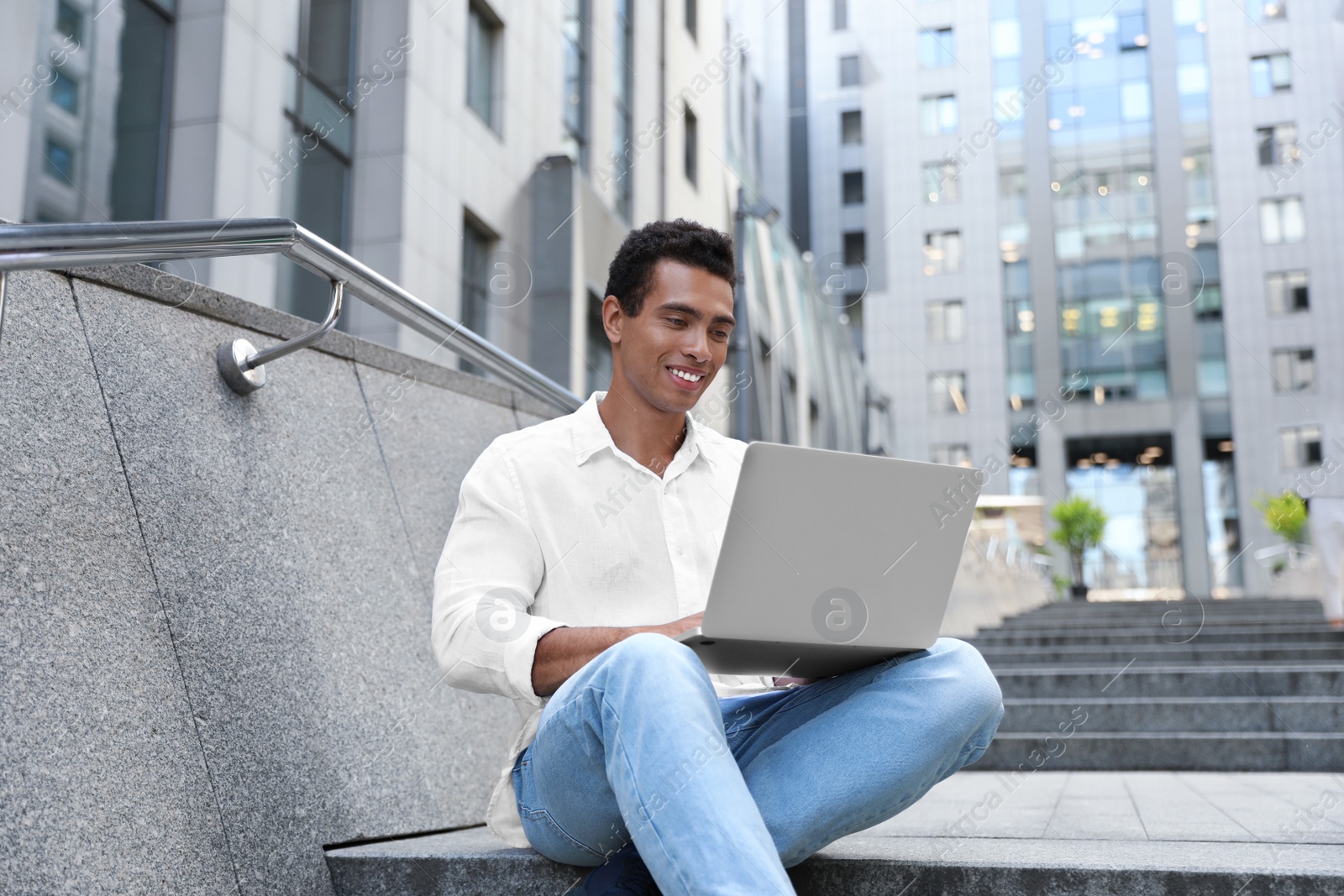 Photo of Handsome young African-American man with laptop sitting on stairs outdoors