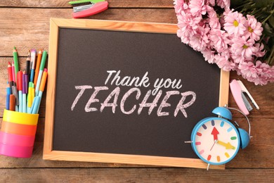 Image of Small blackboard with phrase Thank You Teacher, flowers, alarm clock and different stationery on wooden table, flat lay