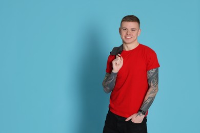 Photo of Smiling young man with tattoos on light blue background. Space for text