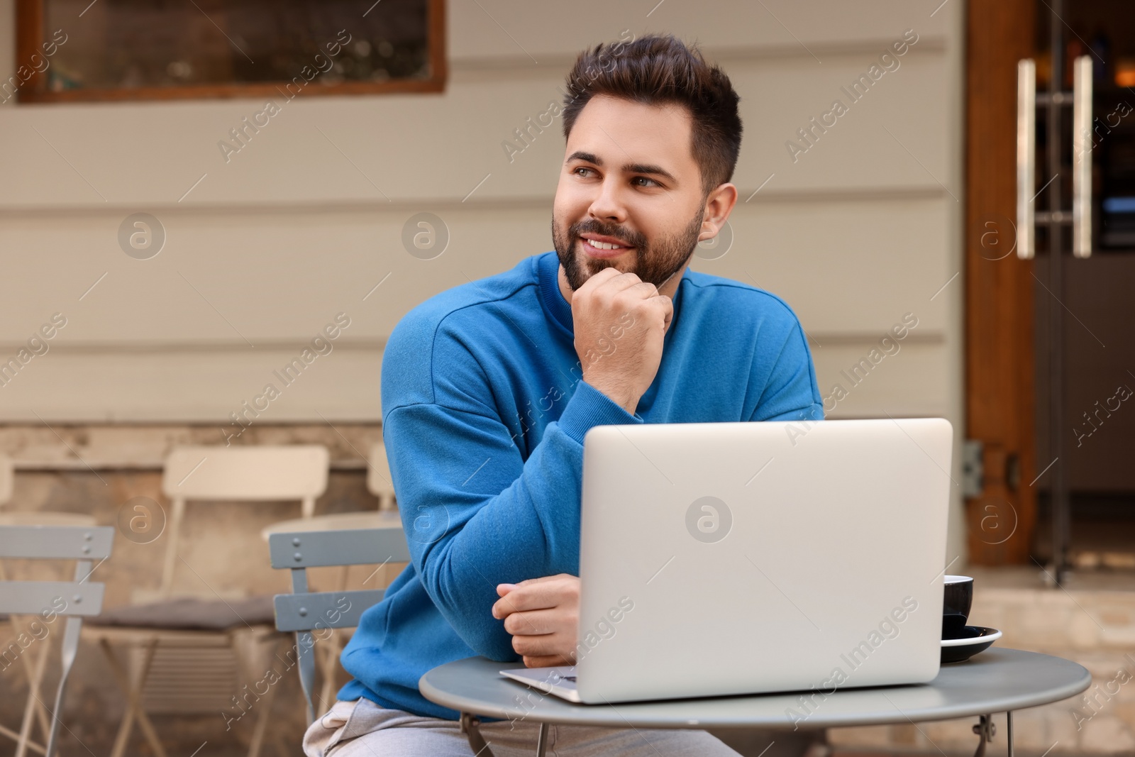 Photo of Handsome young man with laptop at table in outdoor cafe