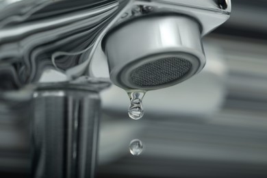 Water drops falling down from tap on blurred background, closeup