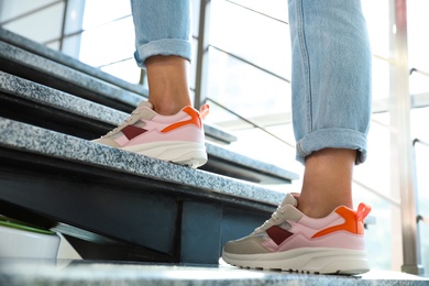 Photo of Young woman wearing stylish sneakers on grey stairs indoors, closeup