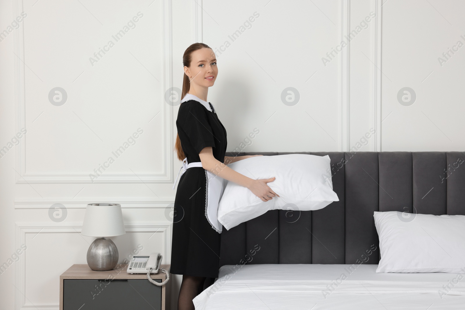 Photo of Young maid making bed in hotel room