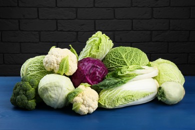 Photo of Many different fresh cabbages on blue wooden table near brick wall