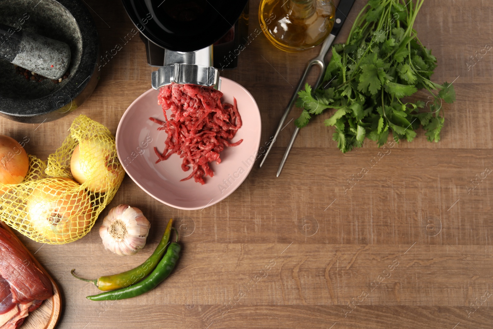 Photo of Mincing beef with electric meat grinder on wooden table, flat lay. Space for text