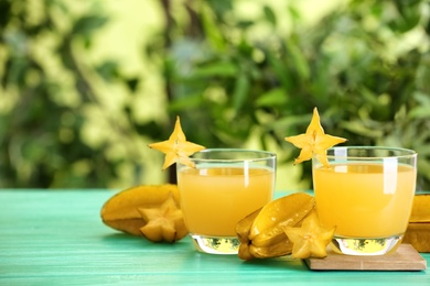 Photo of Delicious carambola juice and fresh fruits on light blue wooden table against blurred background. Space for text