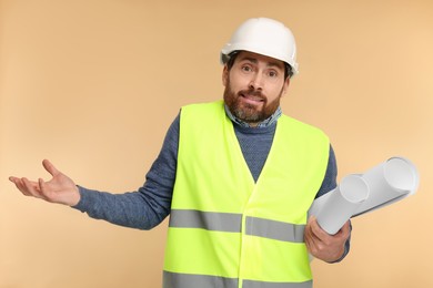 Photo of Confused architect in hard hat with drafts on beige background