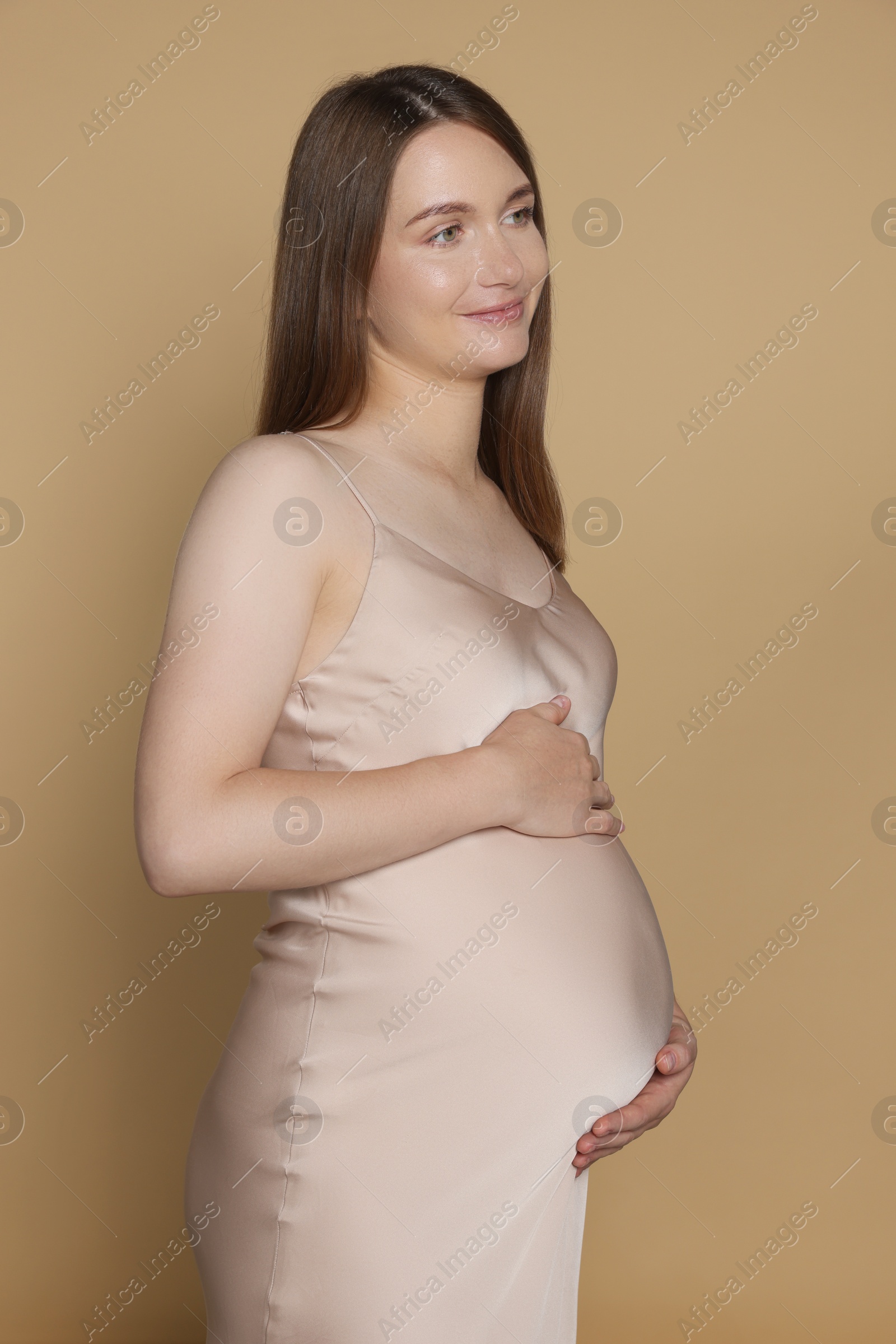 Photo of Happy pregnant woman touching belly on beige background