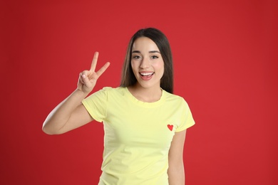 Photo of Woman in yellow t-shirt showing number two with her hand on red background