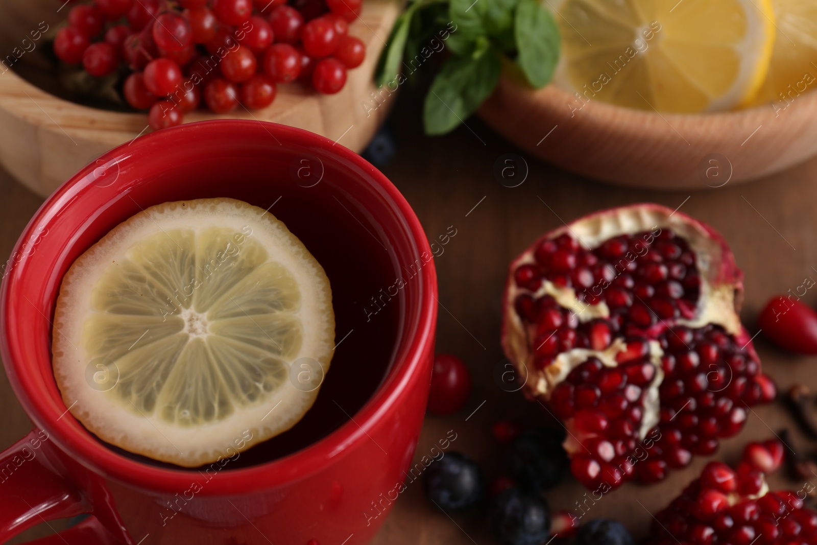 Photo of Cup with delicious immunity boosting tea and ingredients on wooden table, closeup