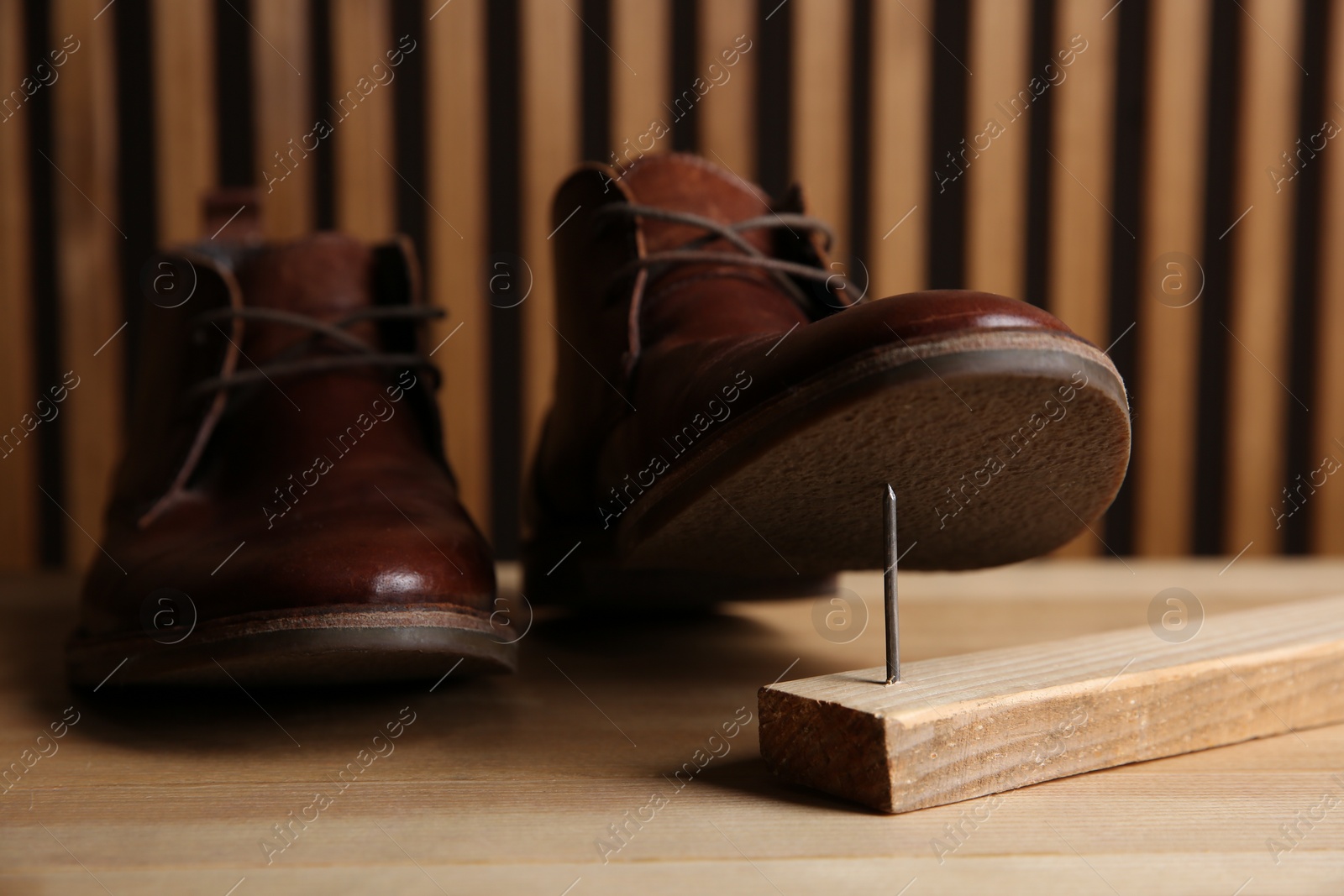 Photo of Metal nail in wooden plank and shoes on table