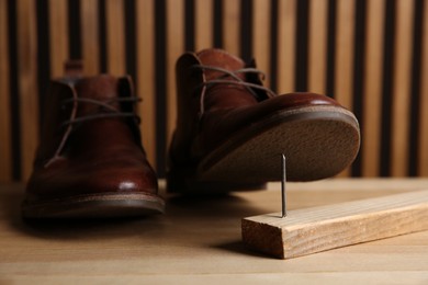 Photo of Metal nail in wooden plank and shoes on table