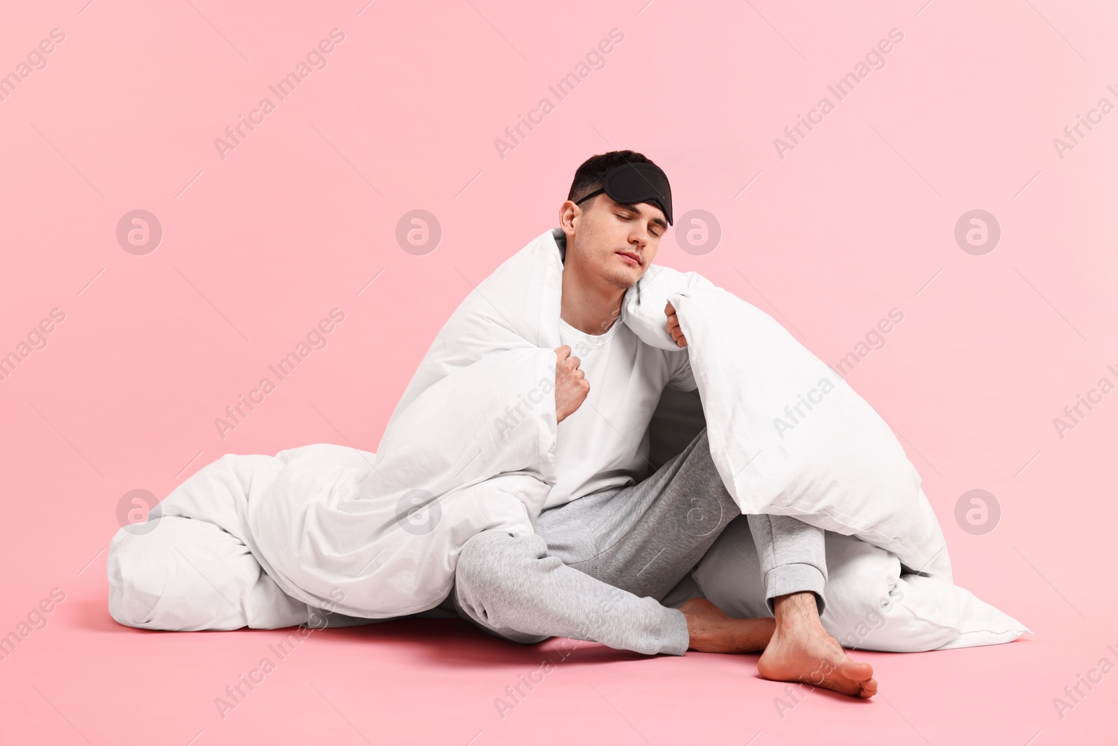 Photo of Man in pyjama and sleep mask wrapped in blanket on pink background