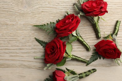 Photo of Many stylish red boutonnieres on light wooden table, flat lay. Space for text