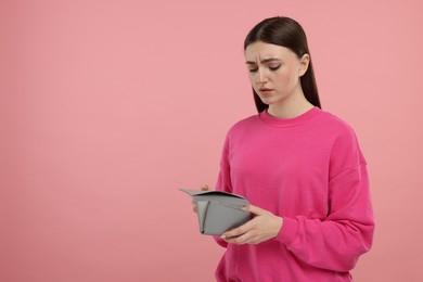 Photo of Sad woman with empty wallet on pink background, space for text