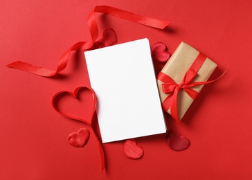 Photo of Flat lay composition with blank greeting card and gift on red background. Valentine's day celebration