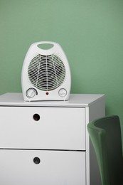 Photo of Modern electric fan heater on chest of drawers indoors