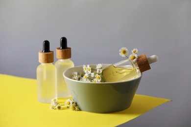 Photo of Bottles of chamomile essential oil and flowers on color background