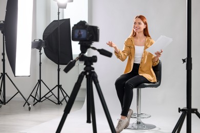 Photo of Casting call. Woman with script performing in front of camera against light grey background at studio