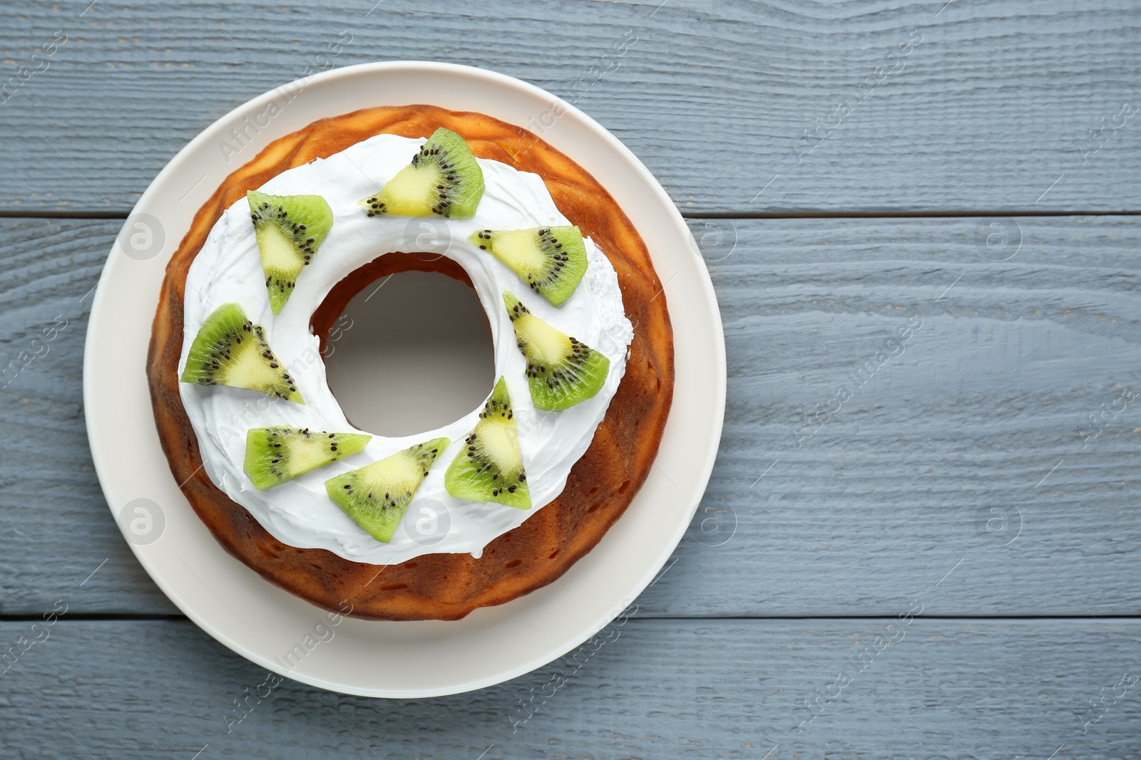 Photo of Homemade yogurt cake with kiwi and cream on grey wooden table, top view. Space for text