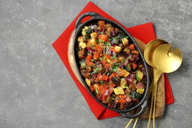 Dish with tasty ratatouille and cutlery on grey textured table, top view. Space for text