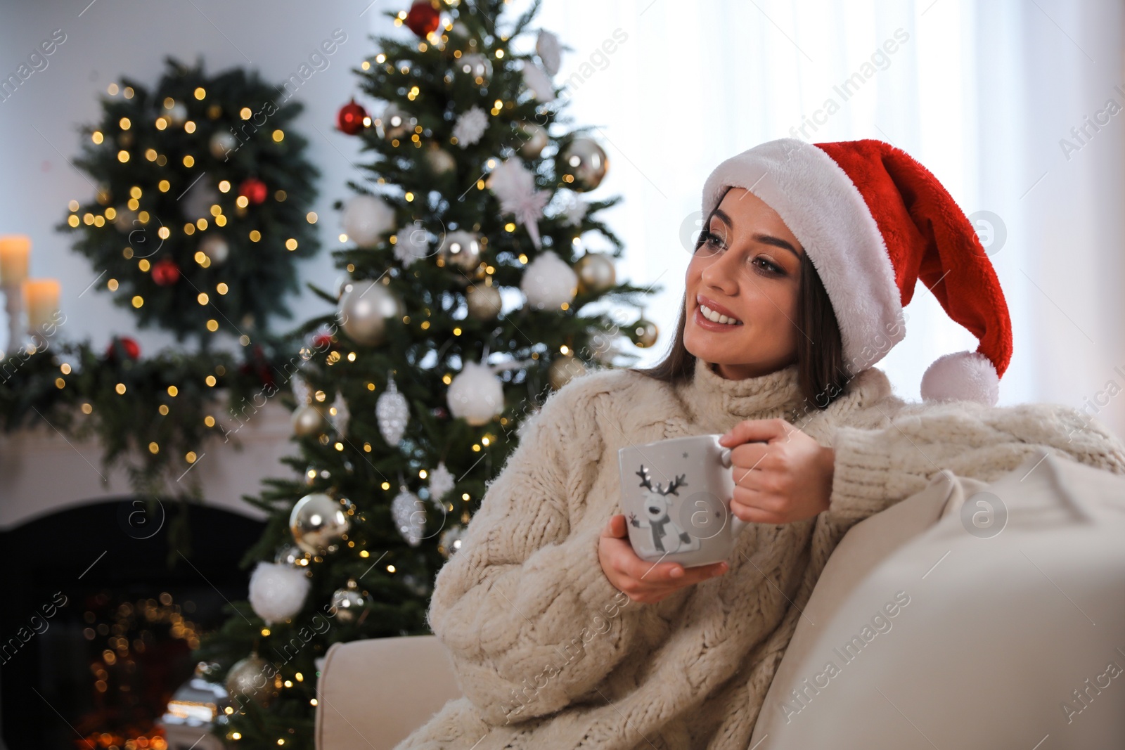 Photo of Beautiful young woman with cup of hot drink in living room decorated for Christmas