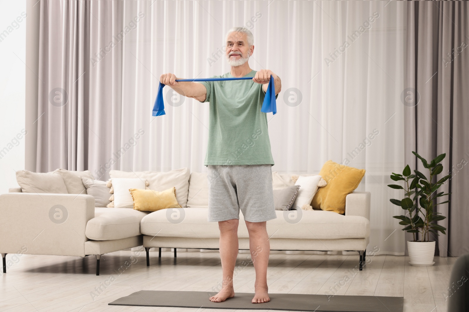 Photo of Senior man doing exercise with fitness elastic band on mat at home