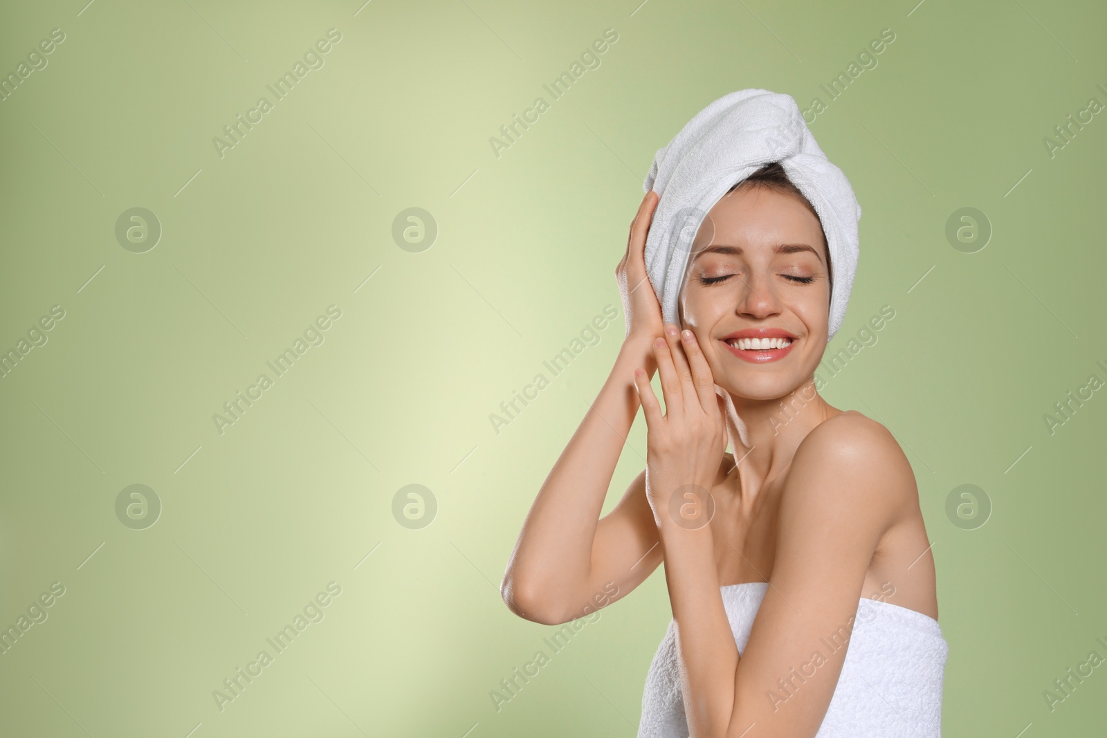 Photo of Beautiful young woman with hair wrapped in towel after washing on light green background. Space for text