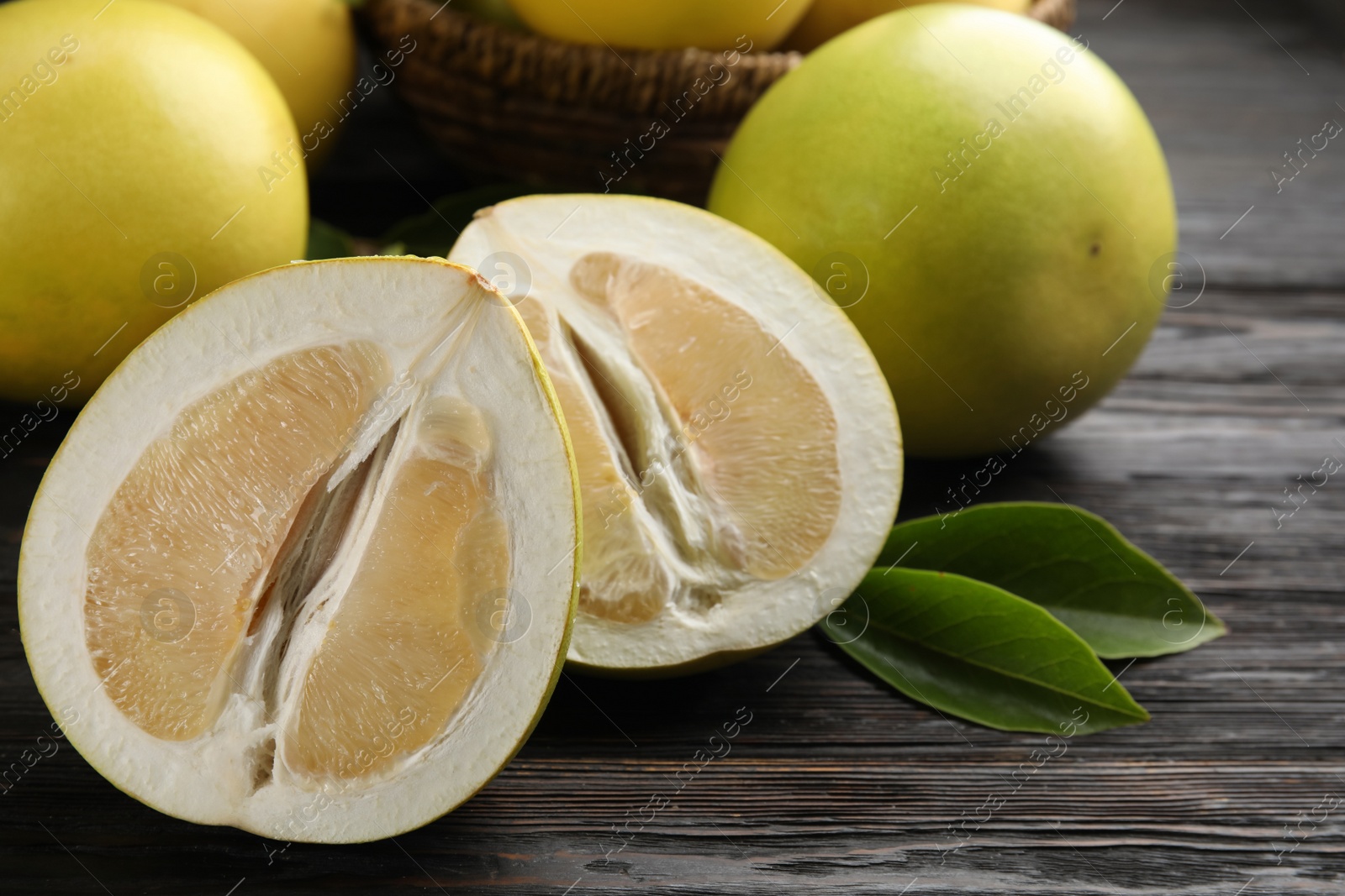 Photo of Fresh cut and whole pomelo fruits on black wooden table, closeup