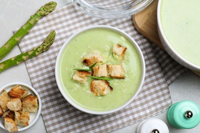 Photo of Bowl of delicious asparagus soup served on light grey table, flat lay