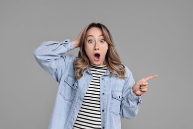 Photo of Portrait of surprised woman pointing at something on grey background