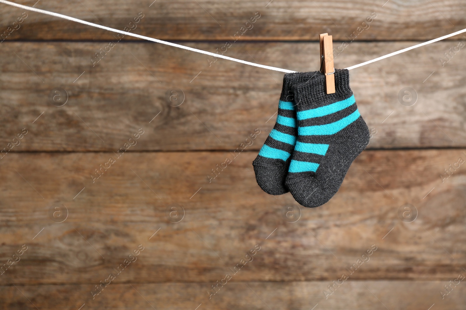 Photo of Pair of socks on laundry line against wooden background, space for text. Baby accessories