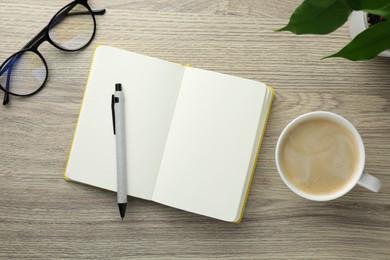 Open notebook, pen, glasses and cup of coffee on wooden table, flat lay. Space for text