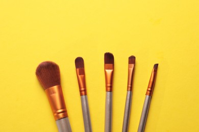 Different makeup brushes on yellow background, flat lay. Space for text