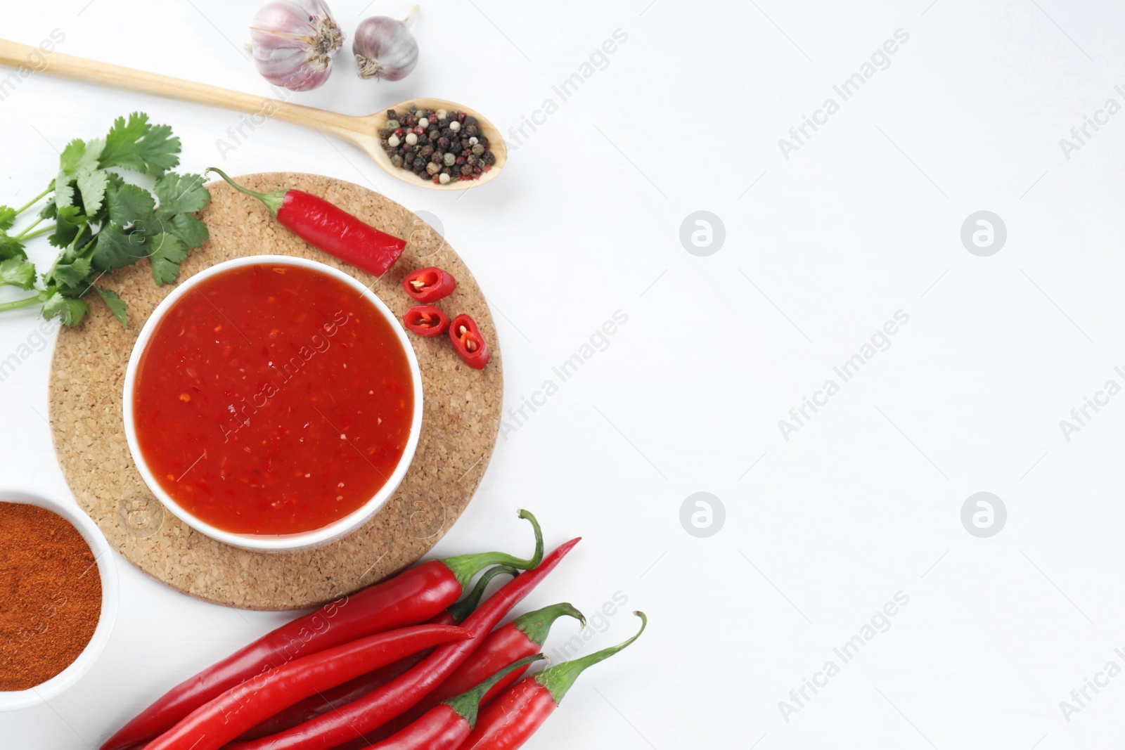 Photo of Spicy chili sauce in bowl and ingredients on white background, flat lay. Space for text