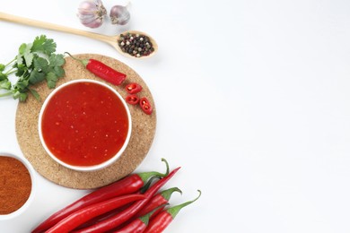 Photo of Spicy chili sauce in bowl and ingredients on white background, flat lay. Space for text