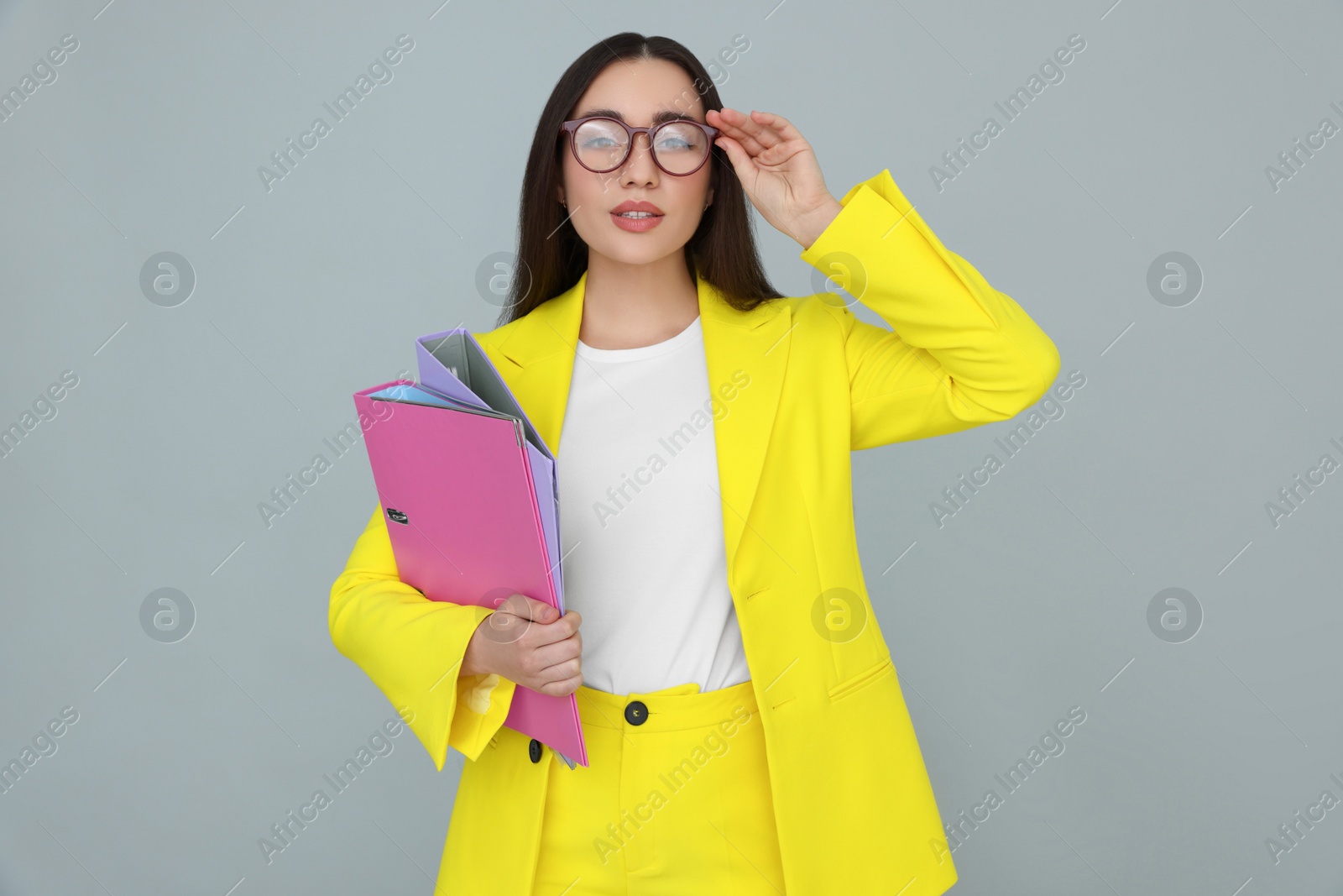 Photo of Young female intern with eyeglasses and folders on grey background