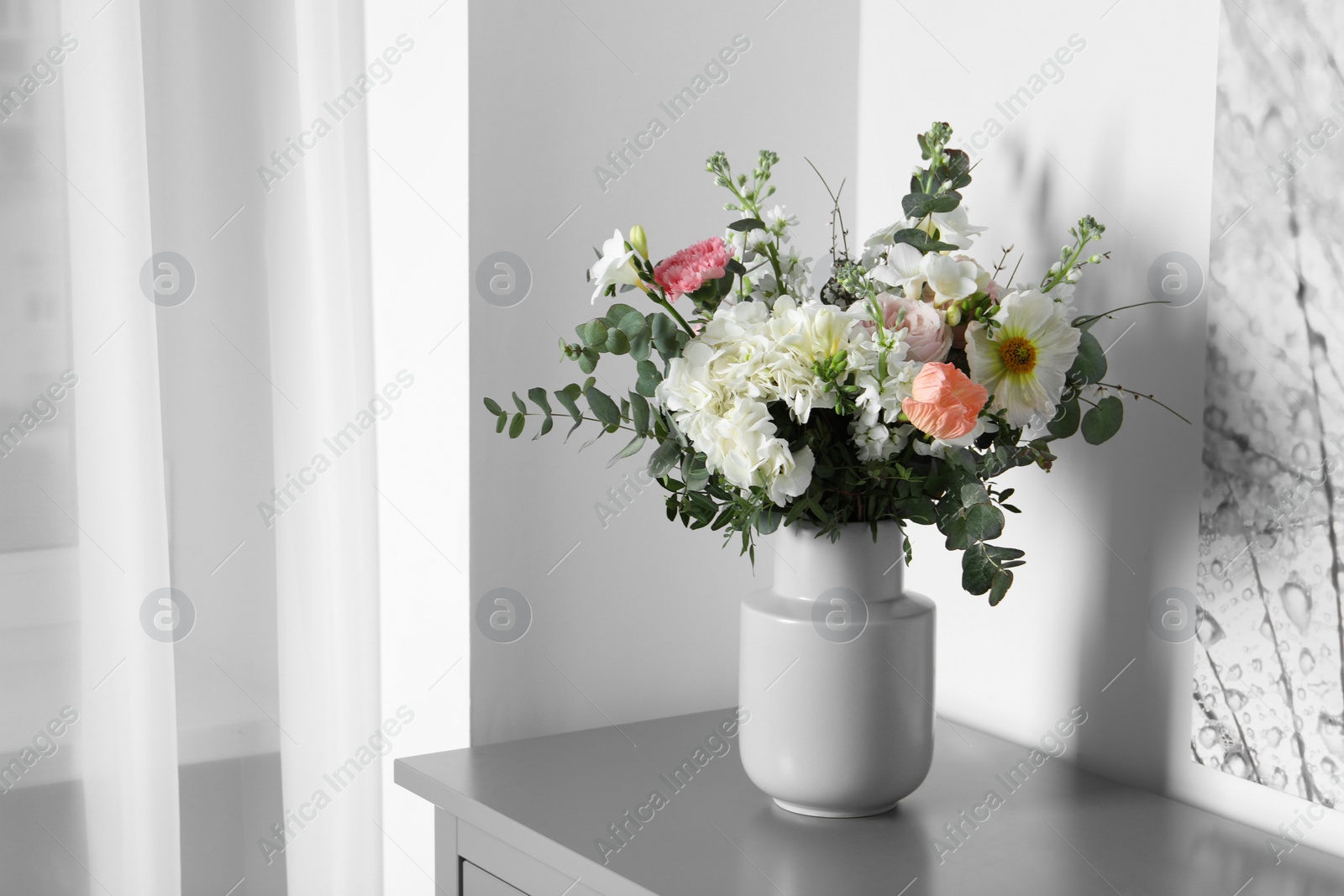 Photo of Bouquet with beautiful flowers on light gray chest of drawers indoors. Space for text