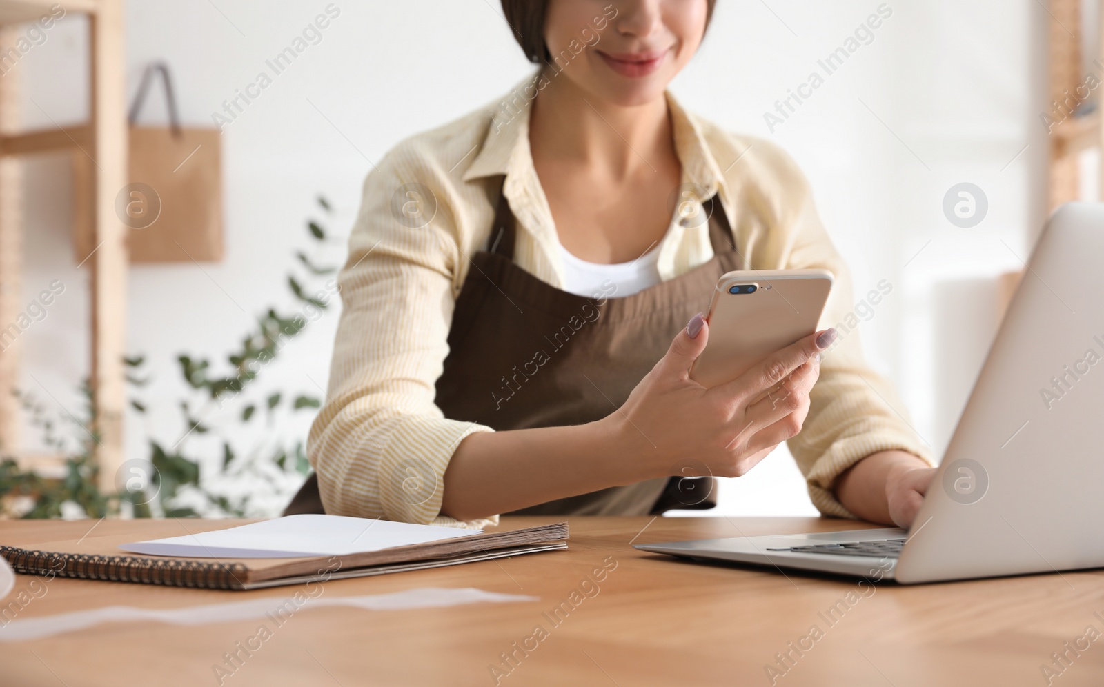 Photo of Florist with smartphone and laptop in workshop, closeup