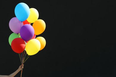 Photo of Woman with bunch of colorful balloons on black background, closeup. Space for text