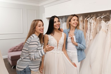 Bride with friends choosing wedding dress in boutique