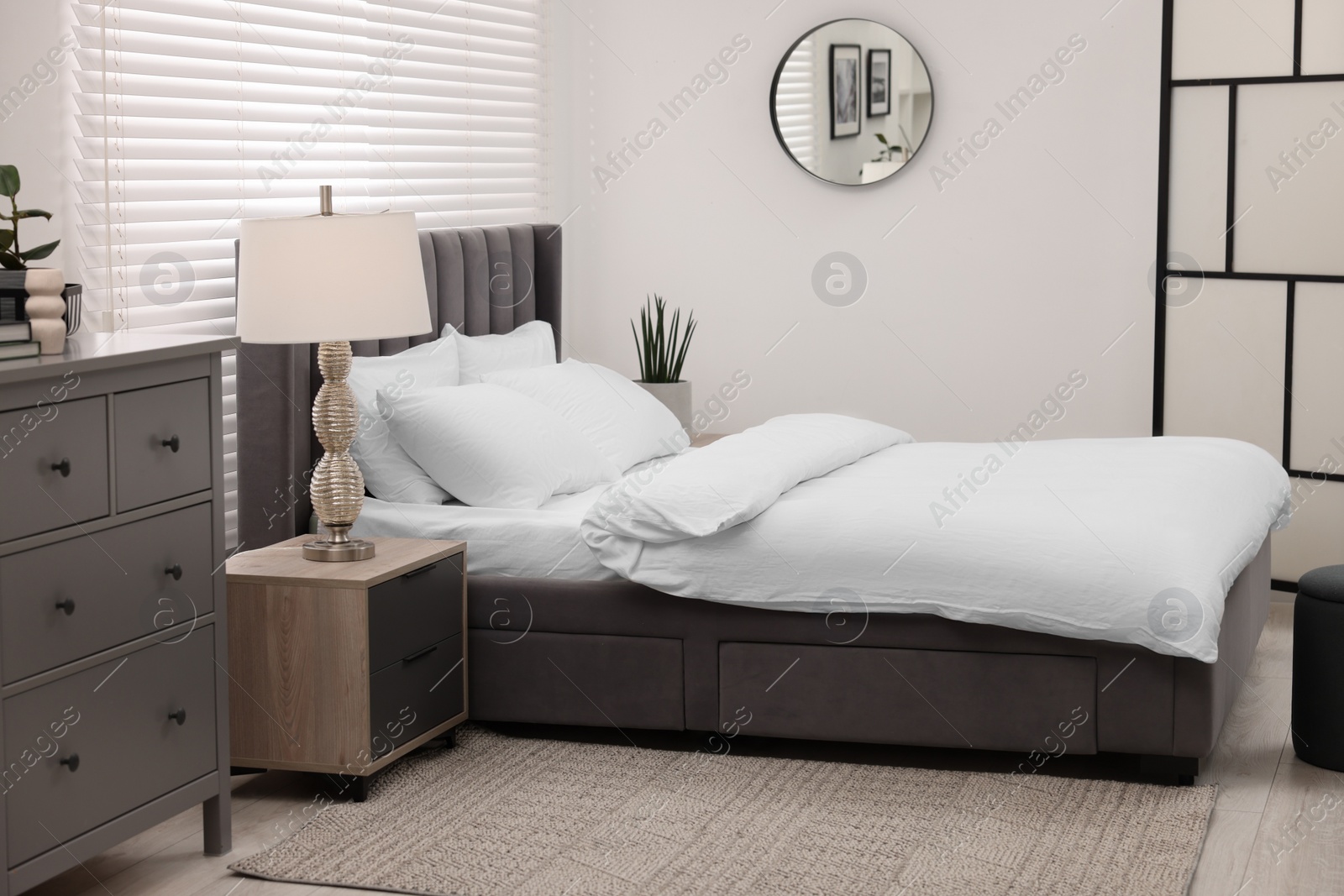 Photo of Stylish bedroom interior with large bed, chest of drawers and lamp