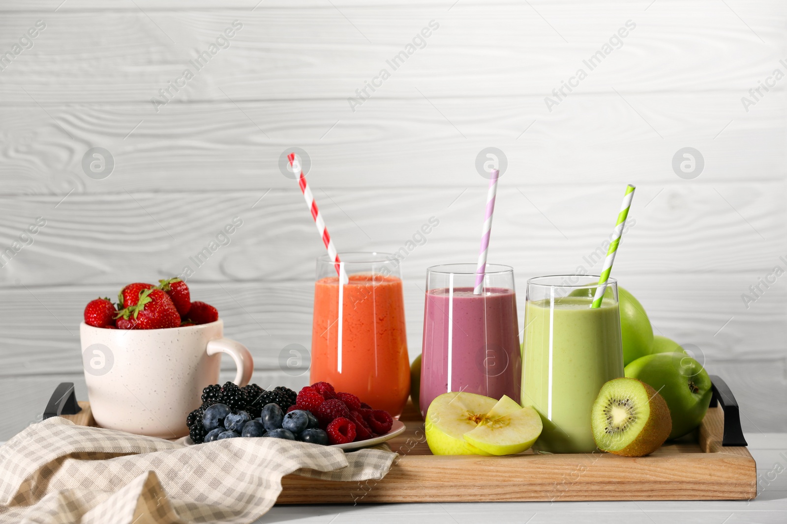 Photo of Glasses of different tasty smoothies and fresh ingredients on white wooden table