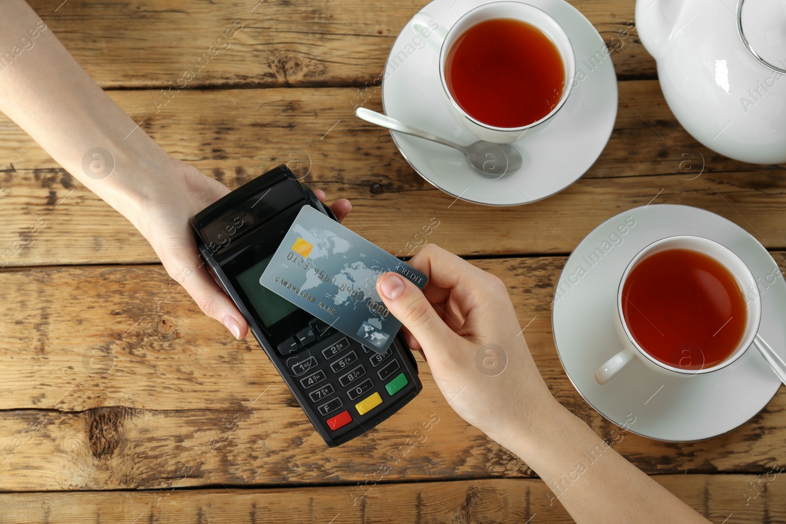 Photo of Woman with credit card using modern payment terminal at wooden table, top view